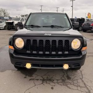 Front view of a black Jeep Renegade with its headlights on in a parking lot.